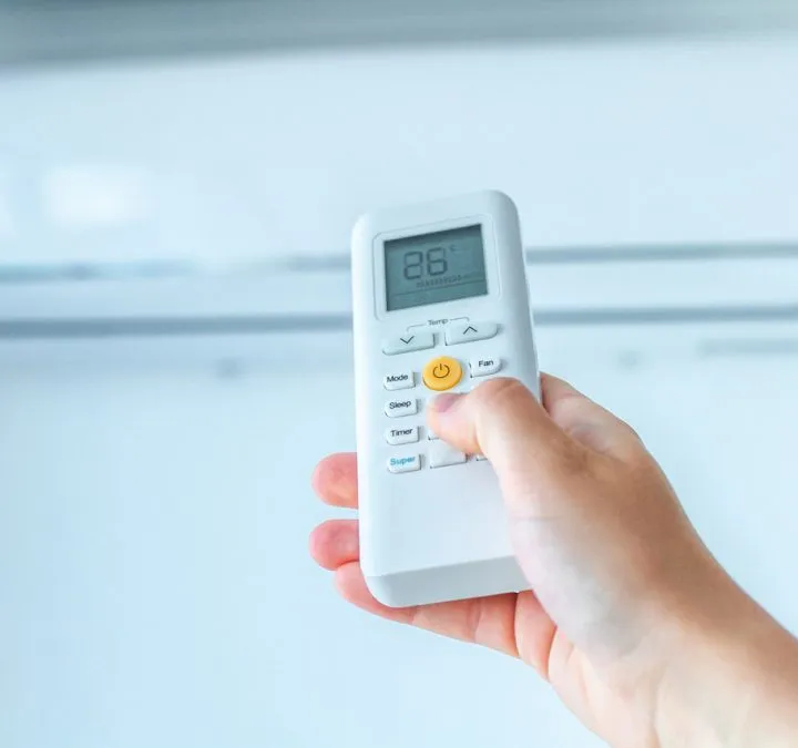 AC Replacement A hand holding an air conditioning remote control to regulate the temperature