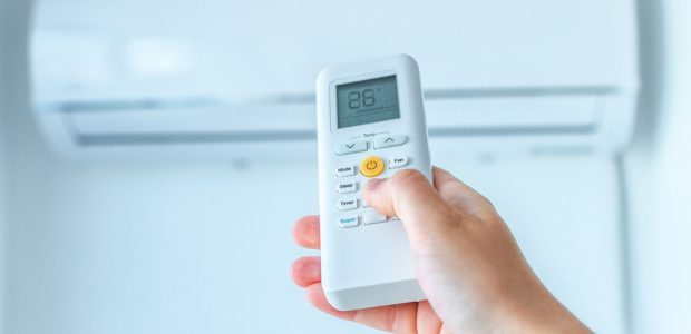 A hand holding an air conditioning remote control to regulate the temperature